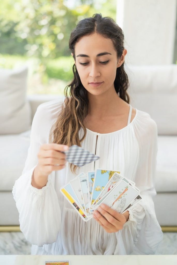 Female in white dress reading tarot cards indoors; a serene moment captured.